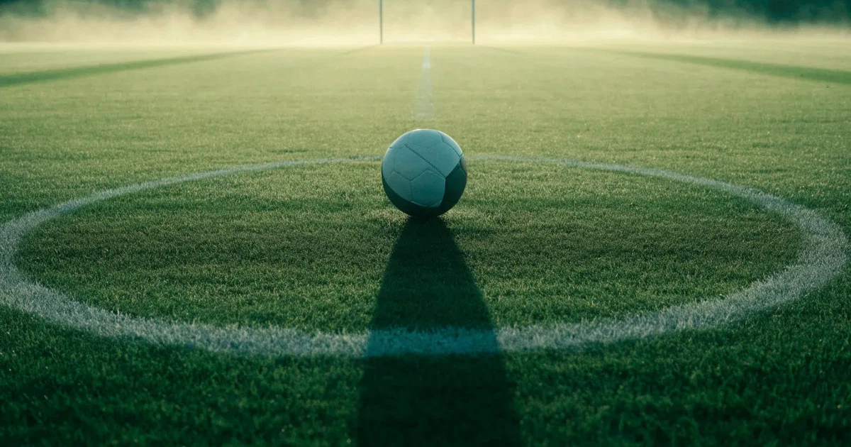 Uma bola de futebol no ponto central de um relvado, à luz da manhã